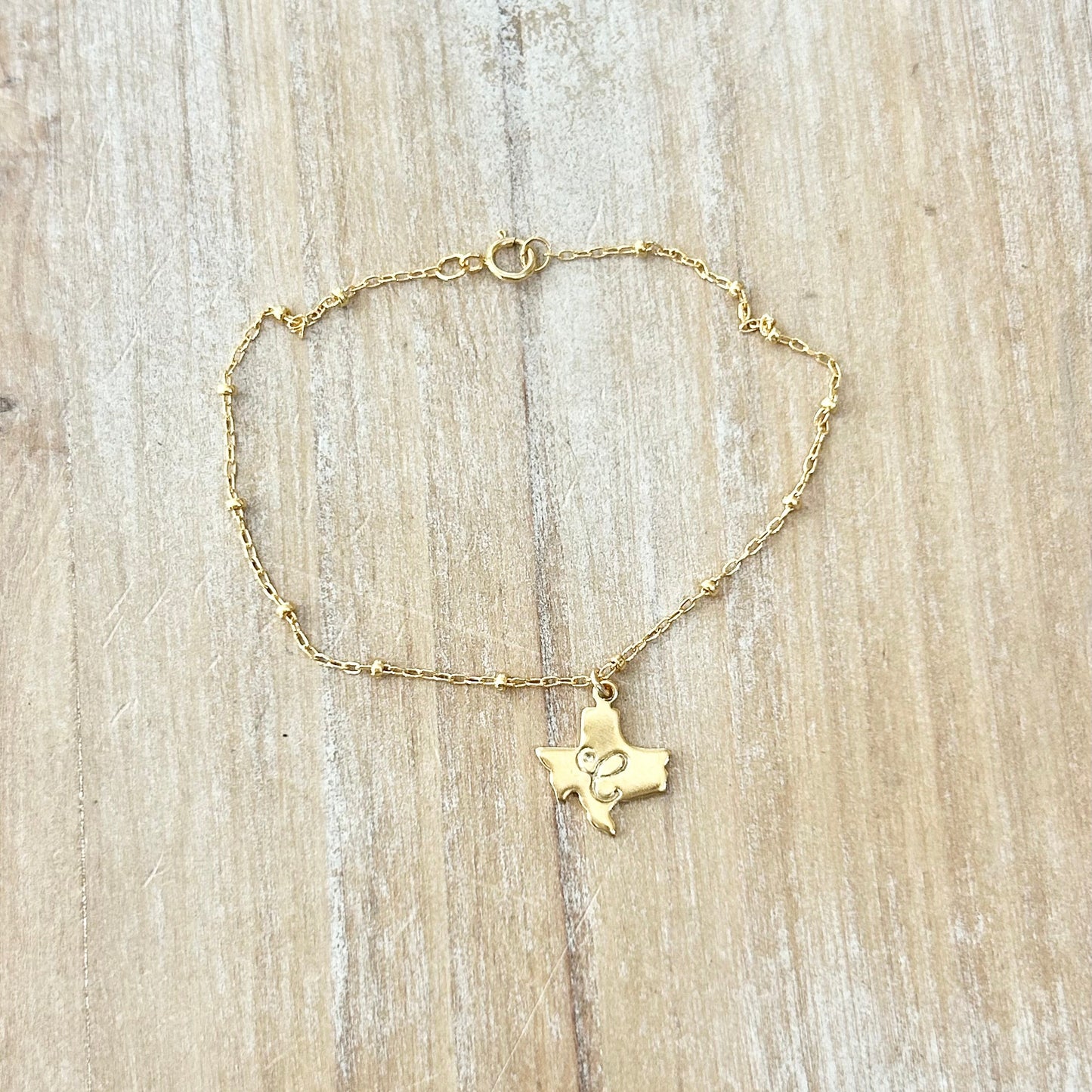 Gold bracelet with a Texas-shaped pendant on a wooden surface