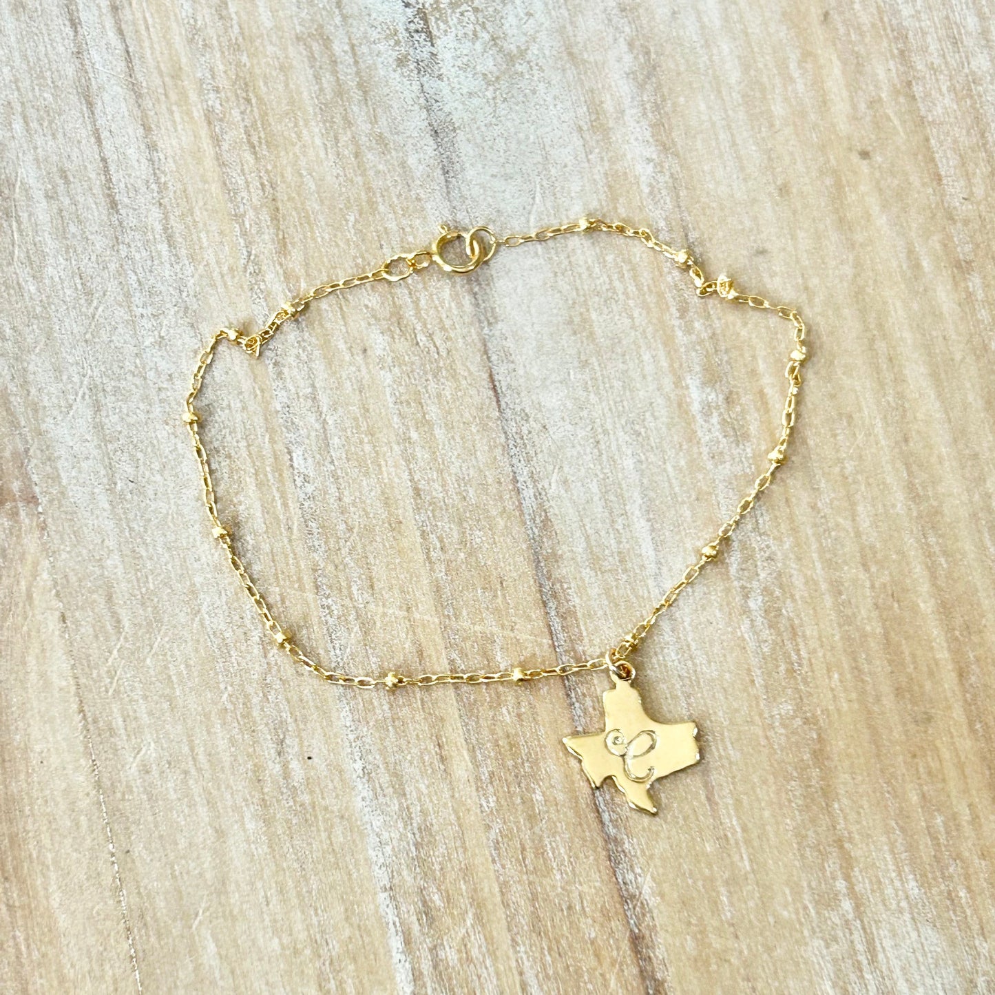 Gold bracelet with a Texas-shaped pendant on a wooden surface