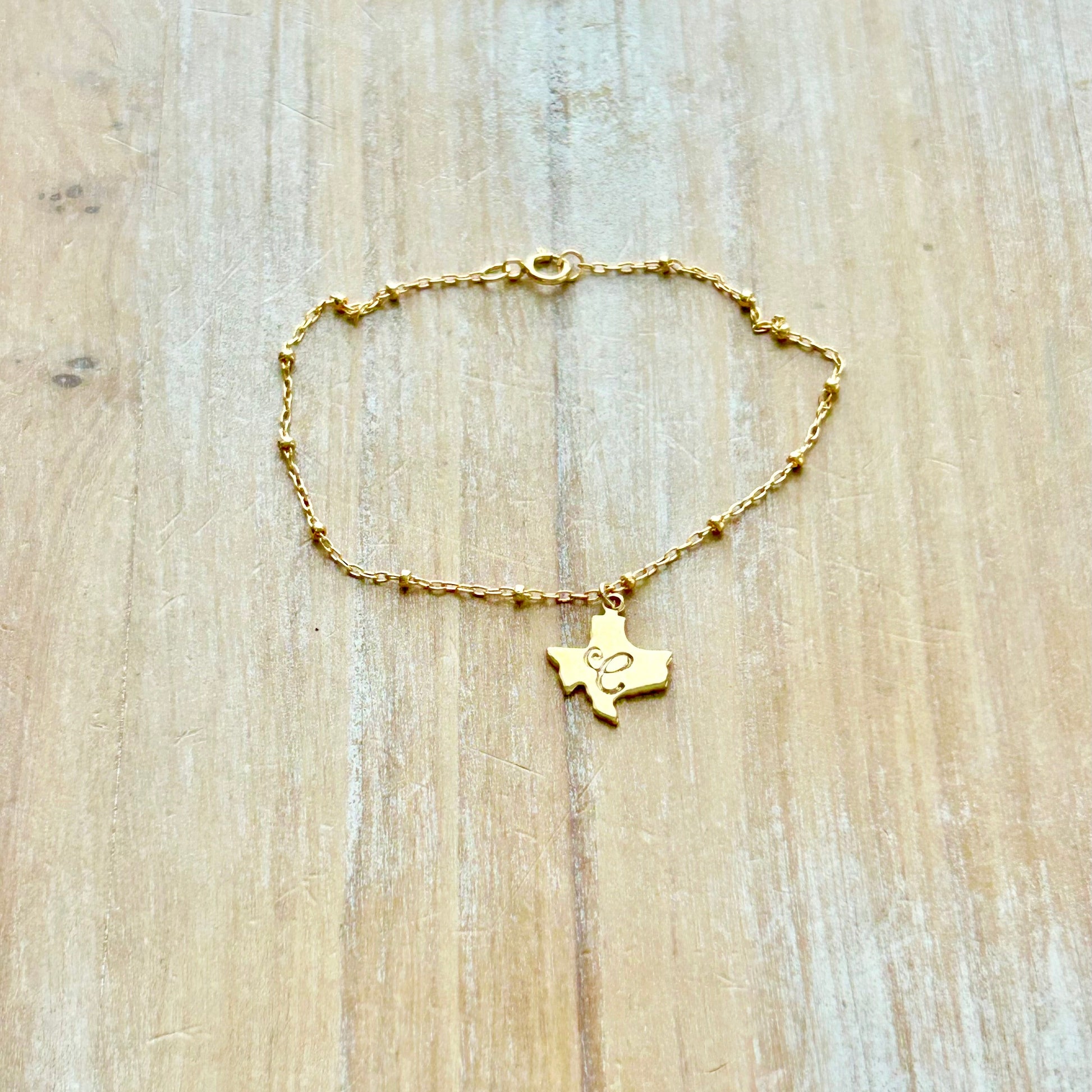 Gold bracelet with a Texas-shaped pendant on a wooden surface