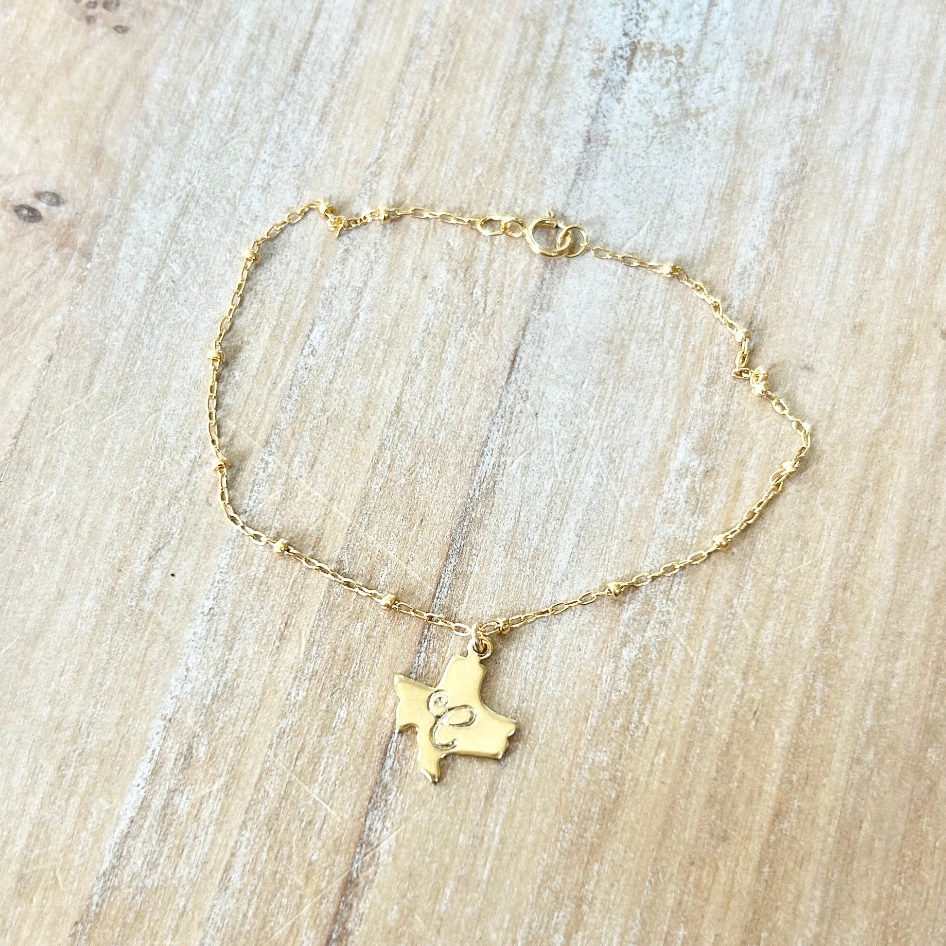 Gold bracelet with a Texas-shaped pendant on a wooden surface