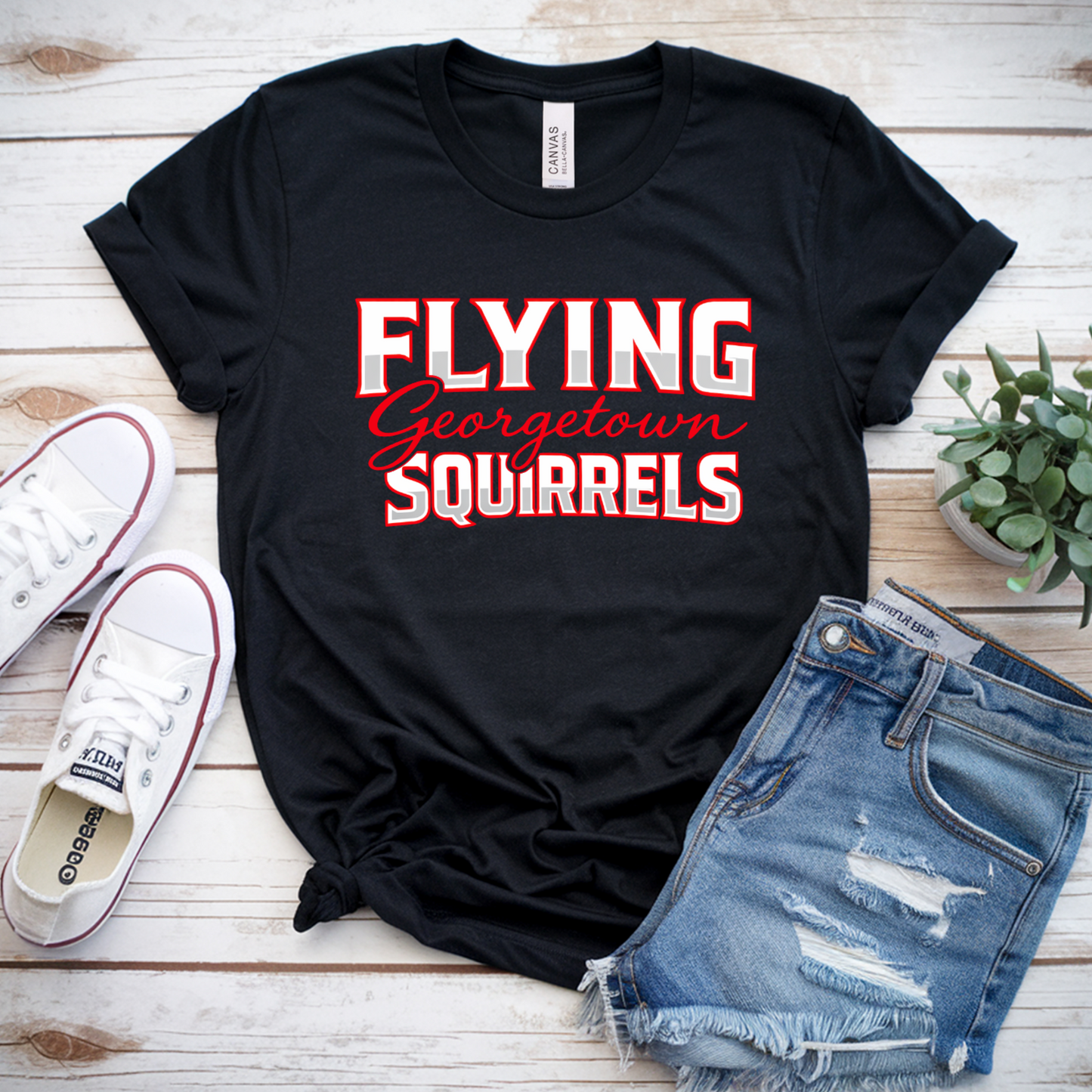 Black t-shirt with 'Flying Georgetown Squirrels' text, paired with jeans and sneakers on a wooden surface.