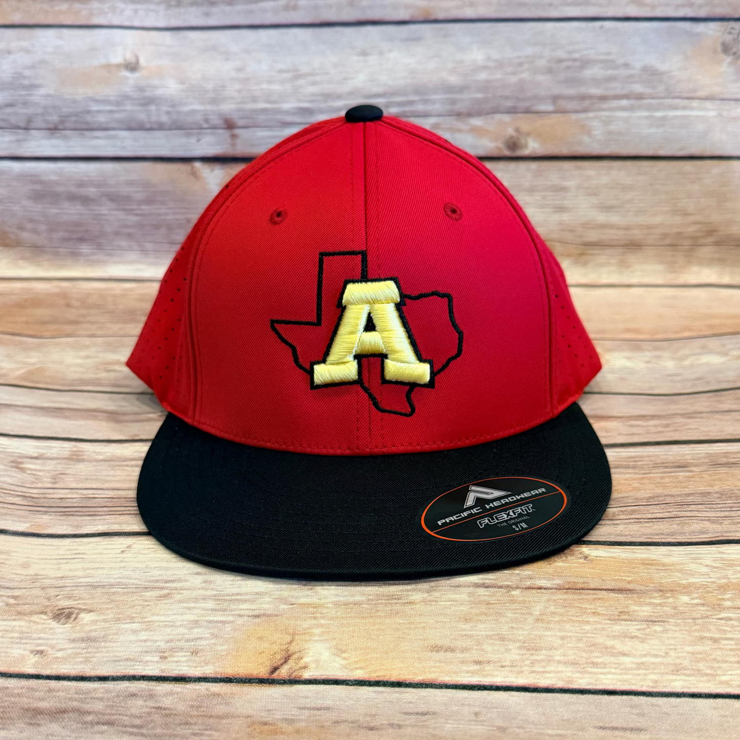 Red and black cap with yellow 'A' logo on a wooden surface