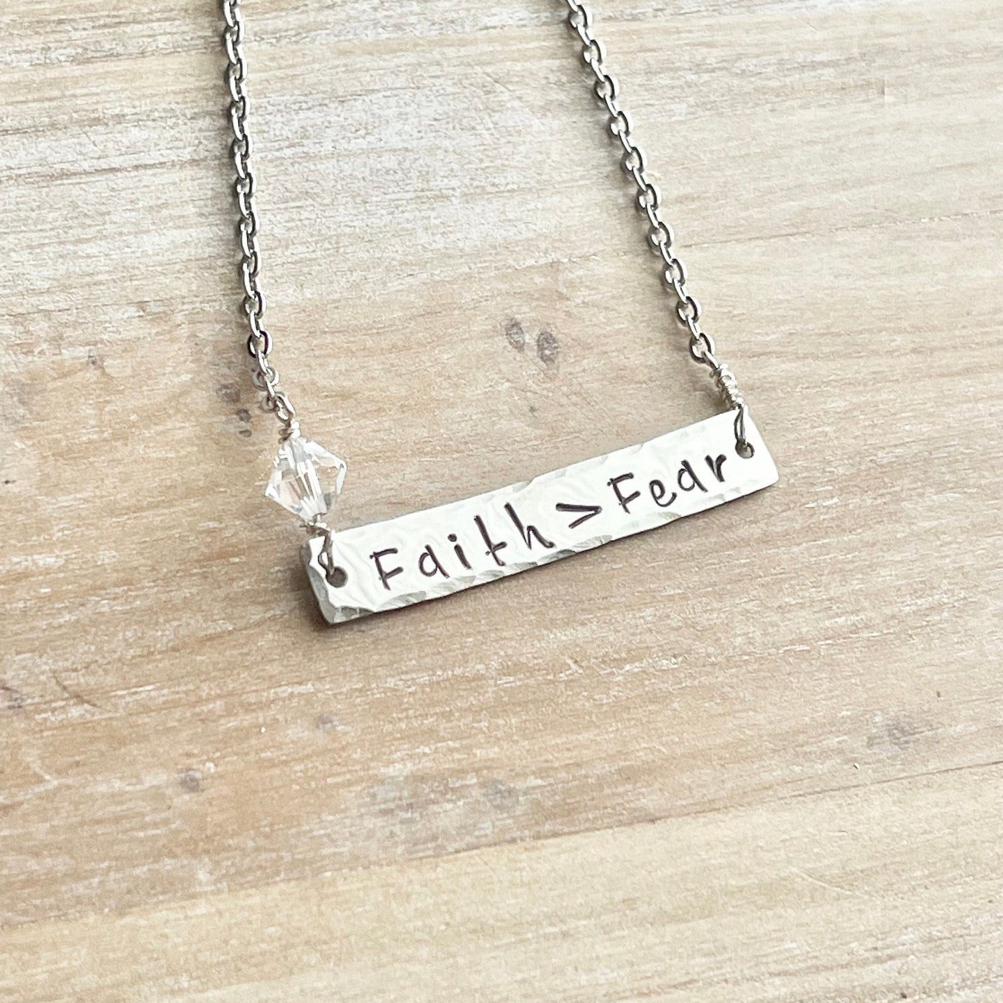 Silver necklace with 'Faith > Fear' pendant on a wooden surface