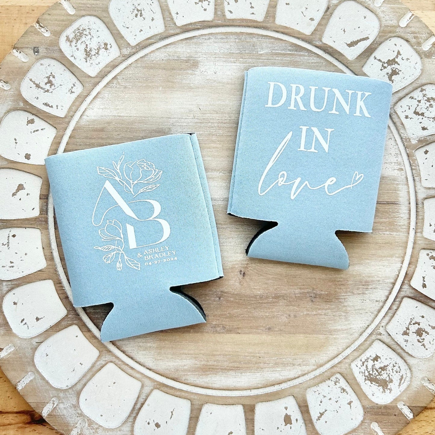 Two blue can coolers with 'Drunk in Love' text on a decorative wooden coaster.