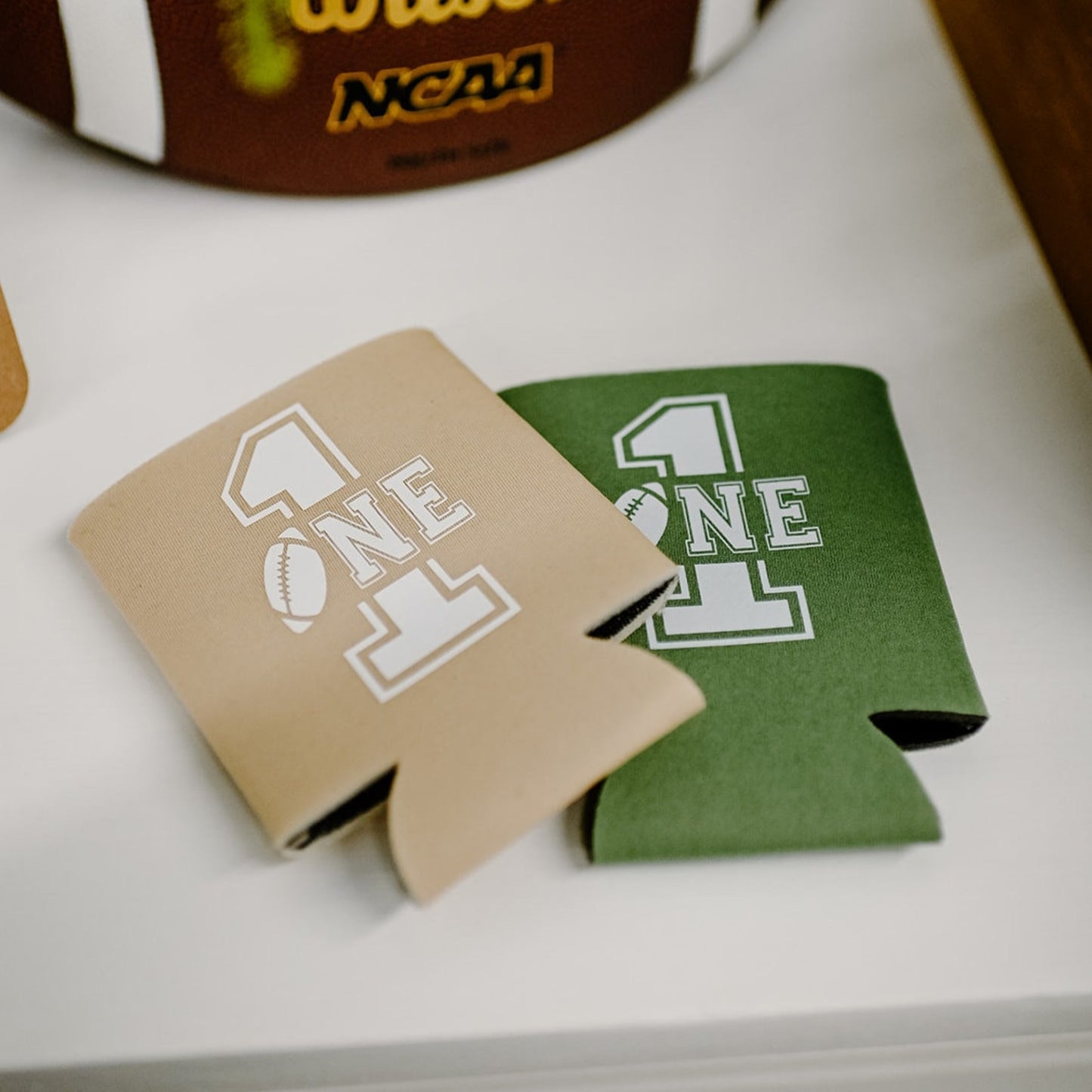 Wilson NCAA football with two can coolers on a white surface