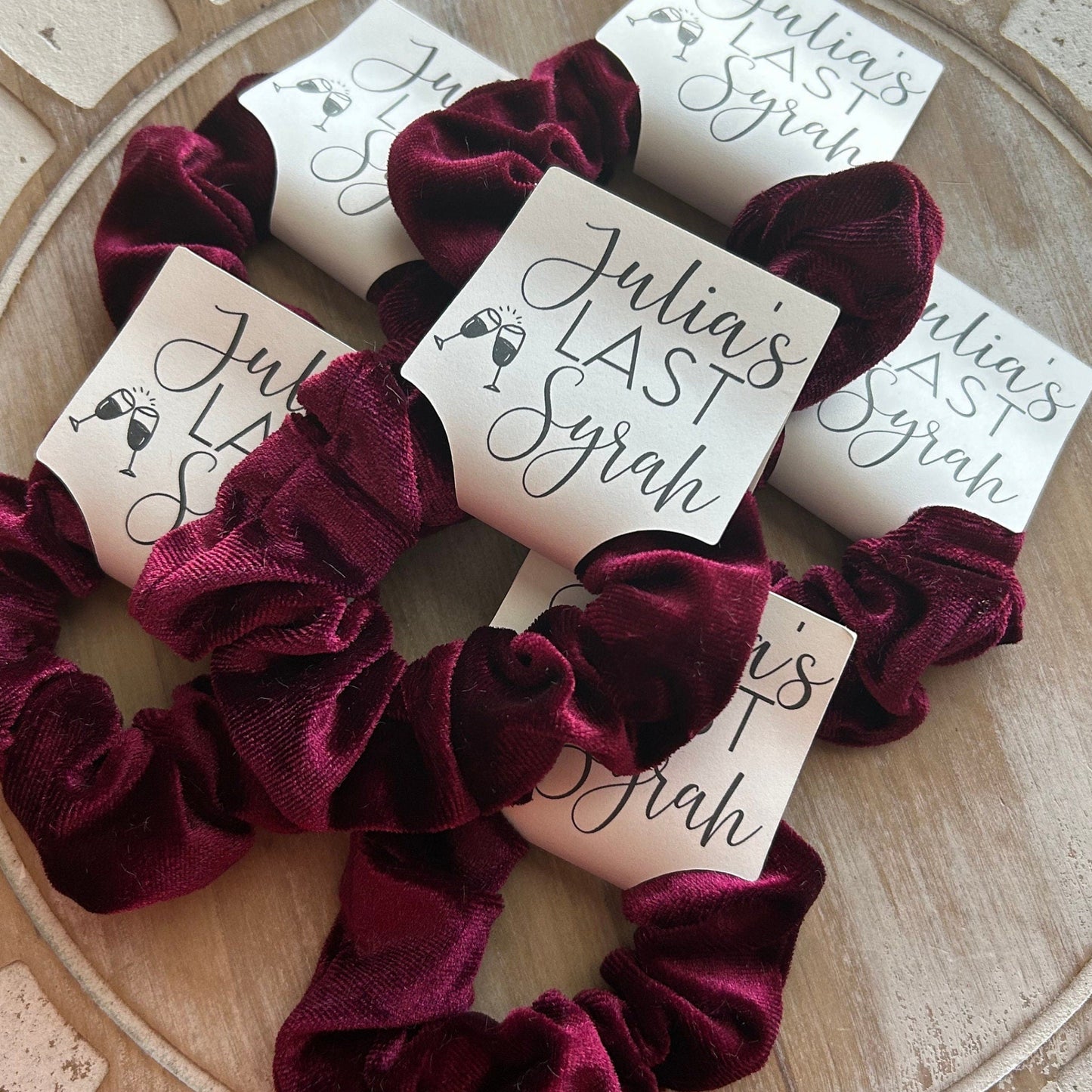 Burgundy scrunchies with 'Julia's Last Syrah' cards on a decorative surface