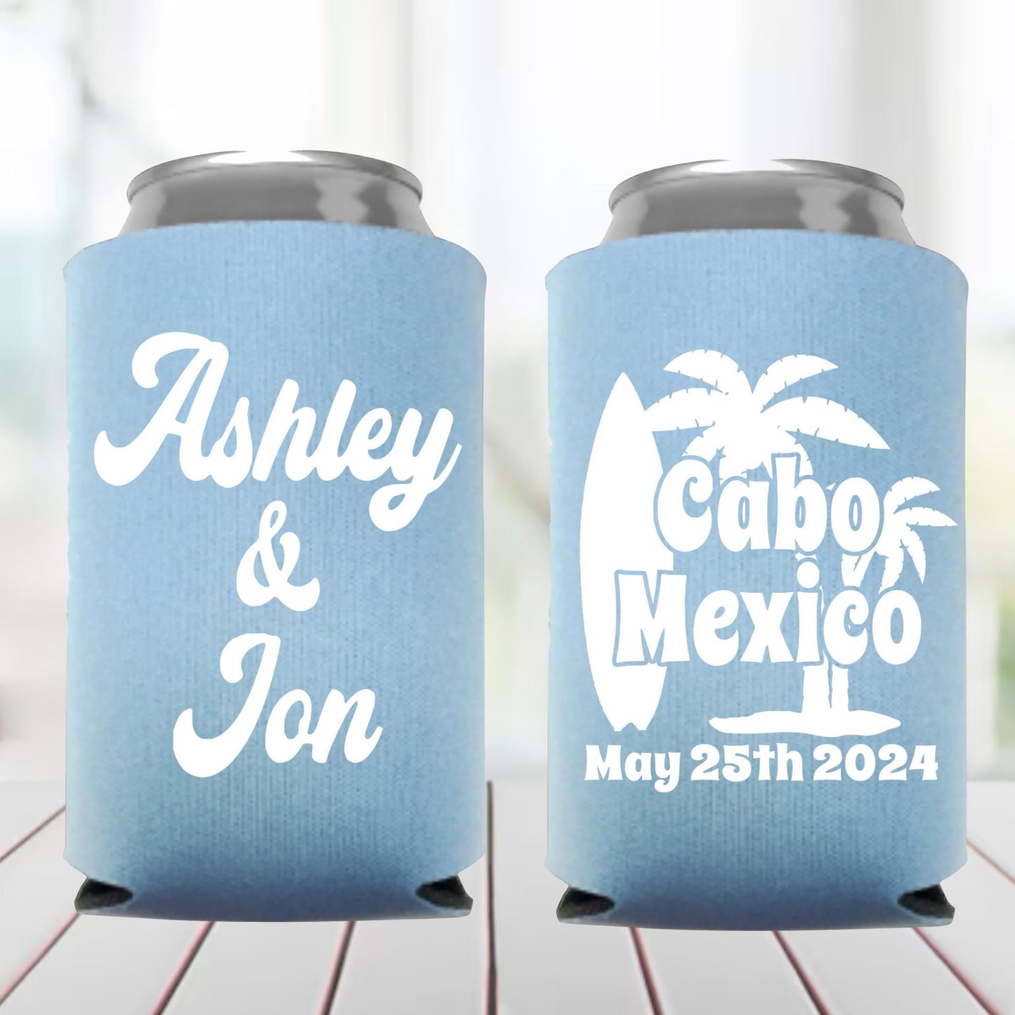 Two light blue can coolers with personalized text on a wooden surface.
