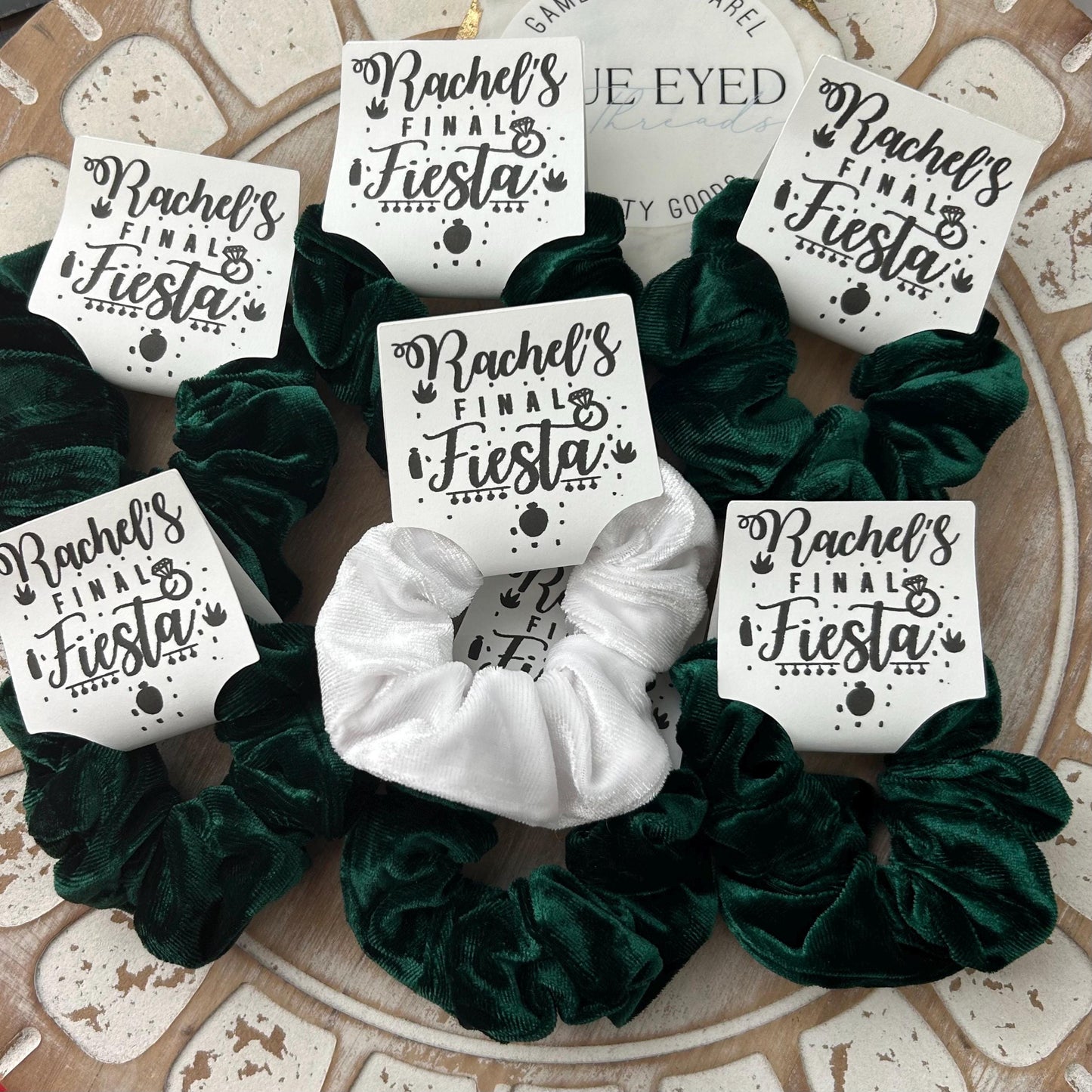 Green and white scrunchies with 'Rachel's Final Fiesta' labels on a patterned surface.