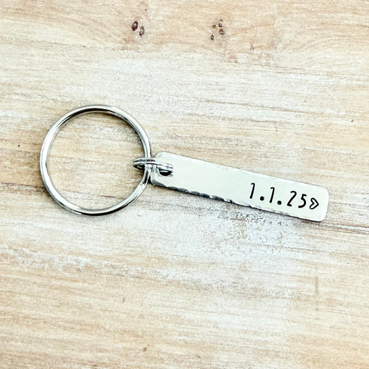 Silver keychain with engraved date on a wooden surface