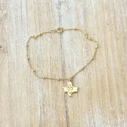 Gold bracelet with a Texas-shaped pendant on a wooden surface
