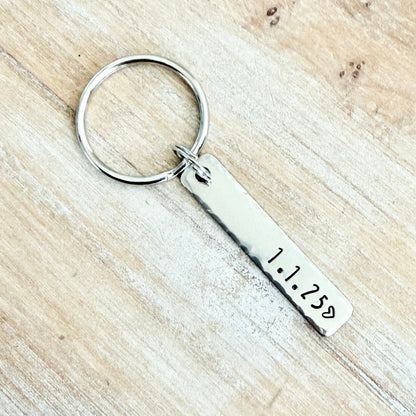 Silver keychain with engraved date on a wooden surface