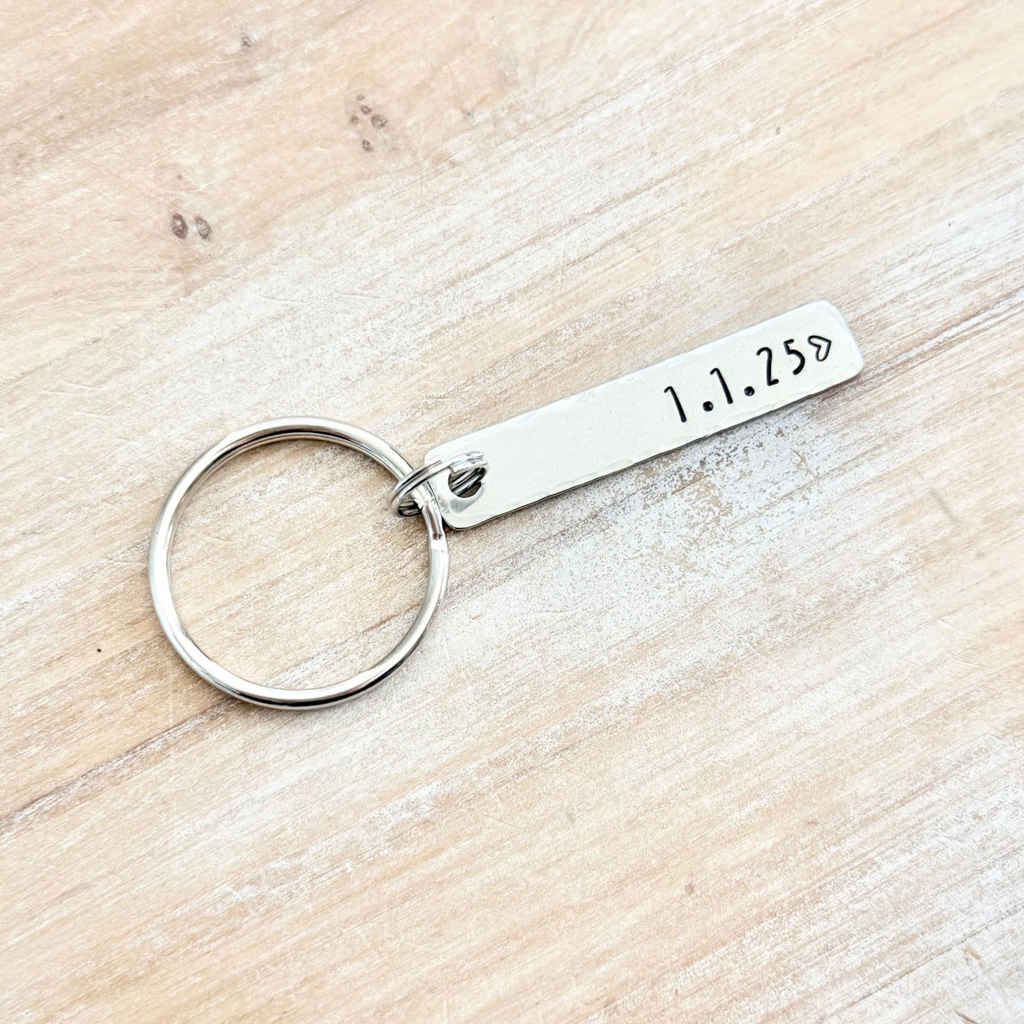 Silver keychain with engraved date on a wooden surface