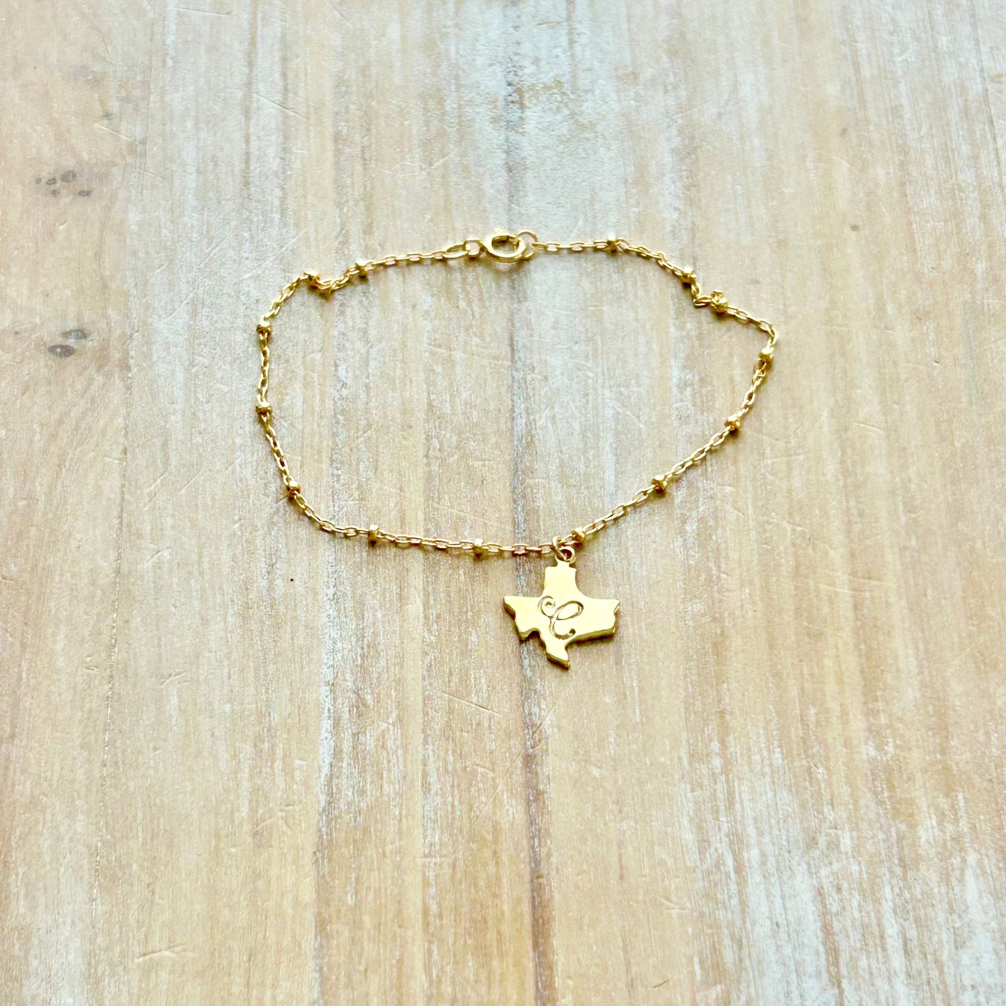 Gold bracelet with a Texas-shaped pendant on a wooden surface