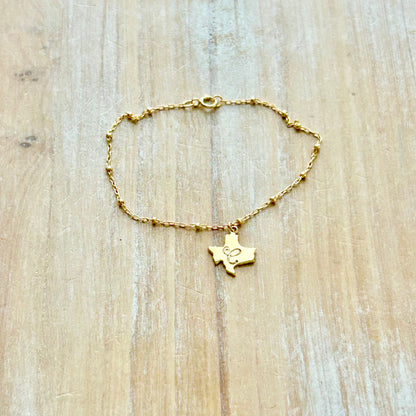 Gold bracelet with a Texas-shaped pendant on a wooden surface