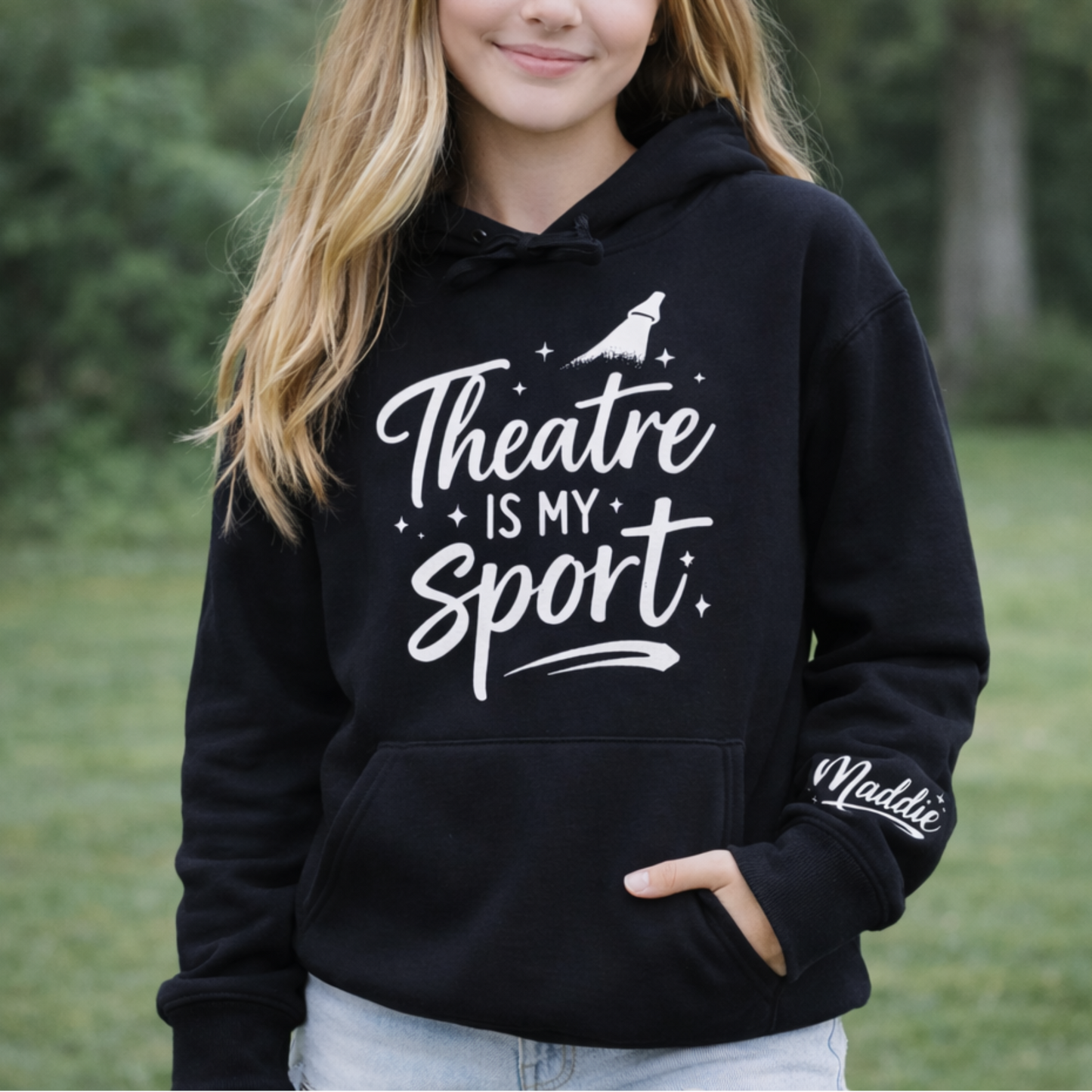 Person wearing a black hoodie with 'Theatre is My Sport' text outdoors.