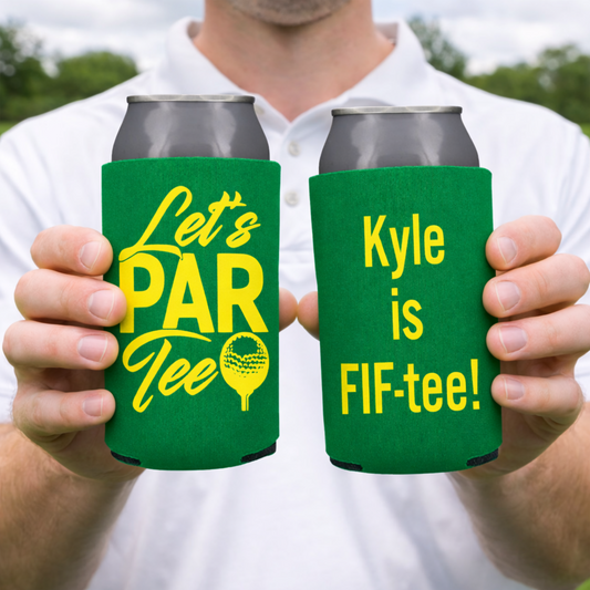 Two green can coolers with yellow text held by a person outdoors.