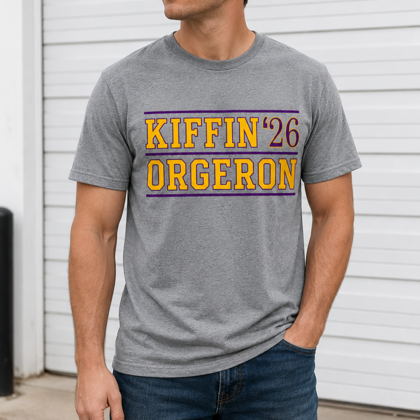 A man wearing a heather gray t-shirt with a yellow and purple graphic that reads 'KIFFIN '26 ORGERON', paired with a black baseball cap and sunglasses, standing in front of a white garage door.