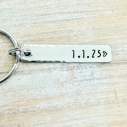 Silver keychain with engraved date '1.1.250' on a wooden surface