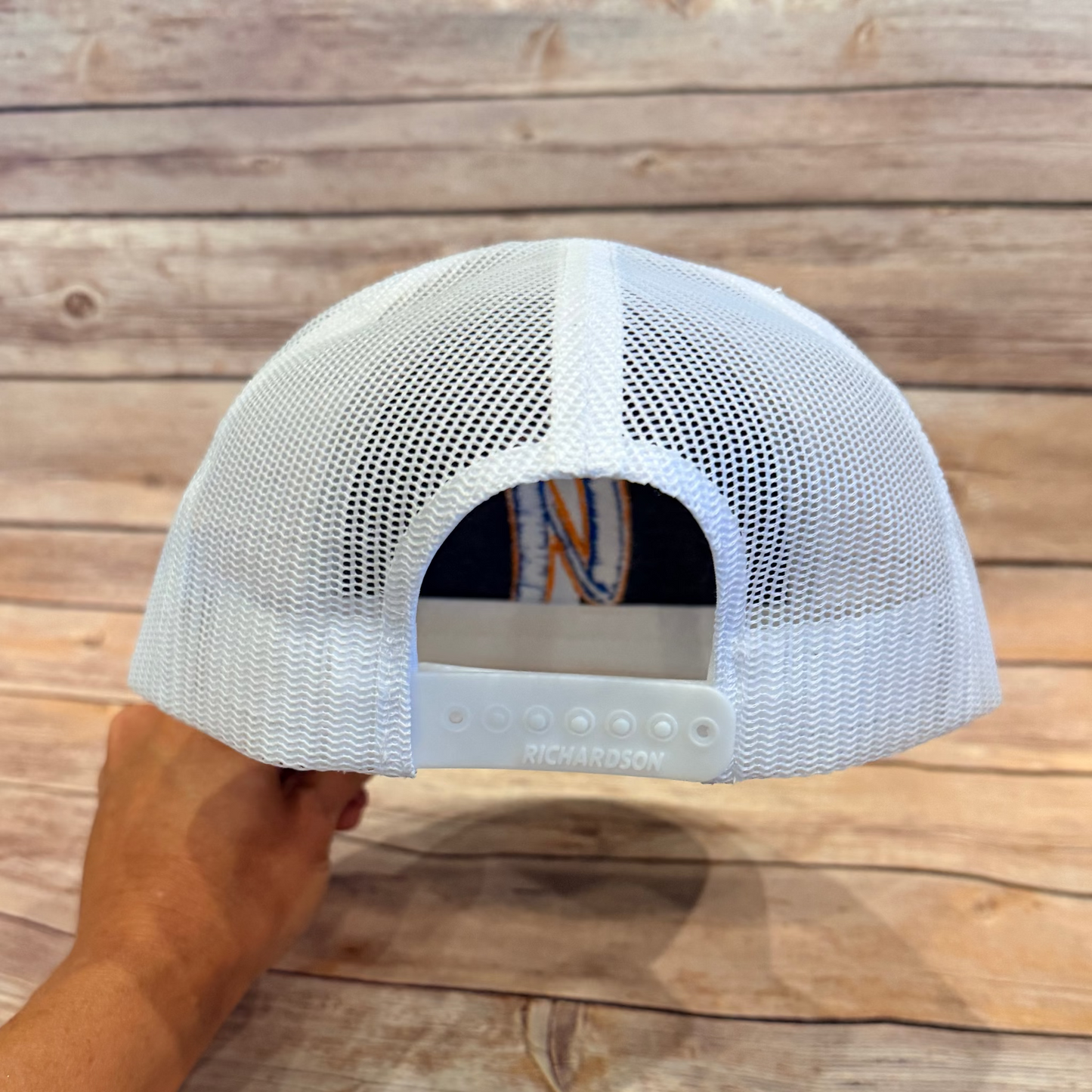 White mesh cap held by a hand on a wooden surface