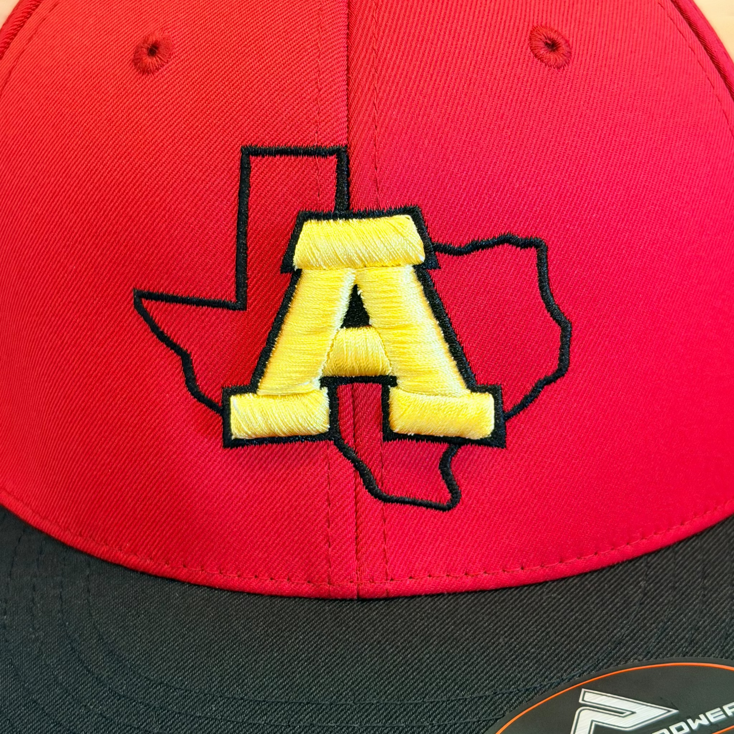 Red and black cap with yellow 'A' logo on a wooden surface