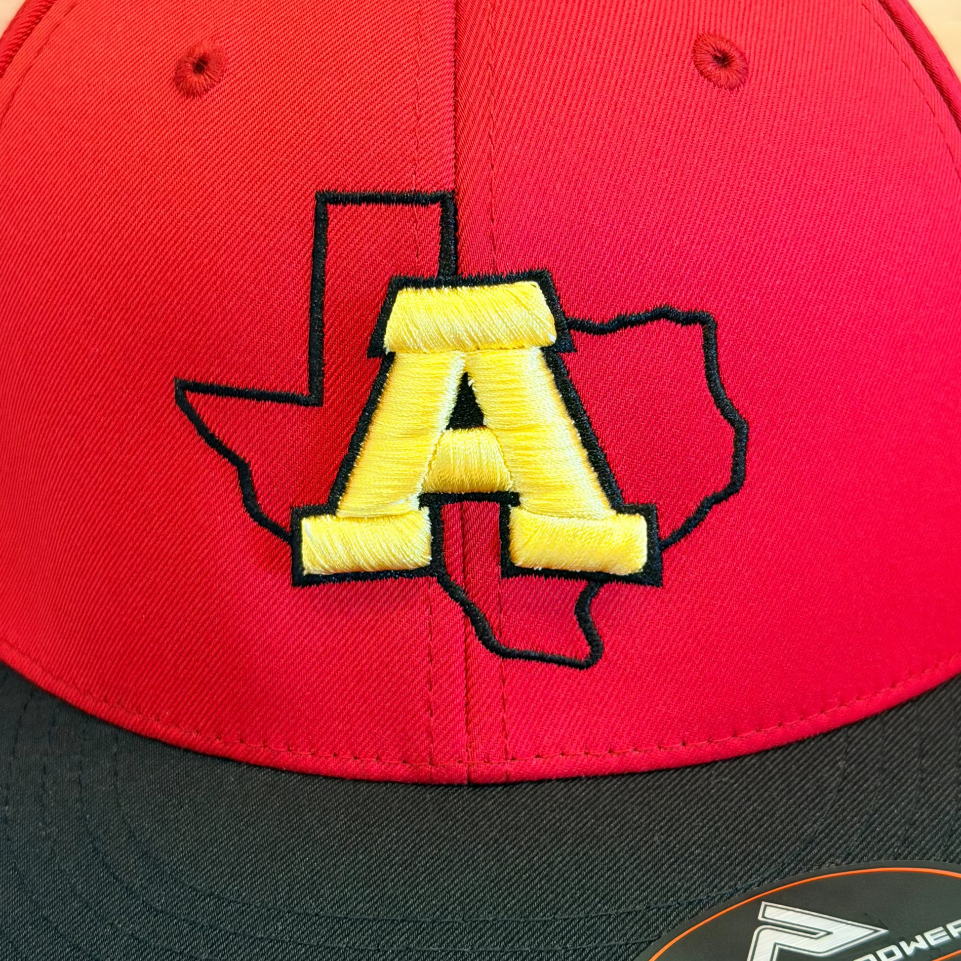 Red and black cap with yellow 'A' logo on a wooden surface