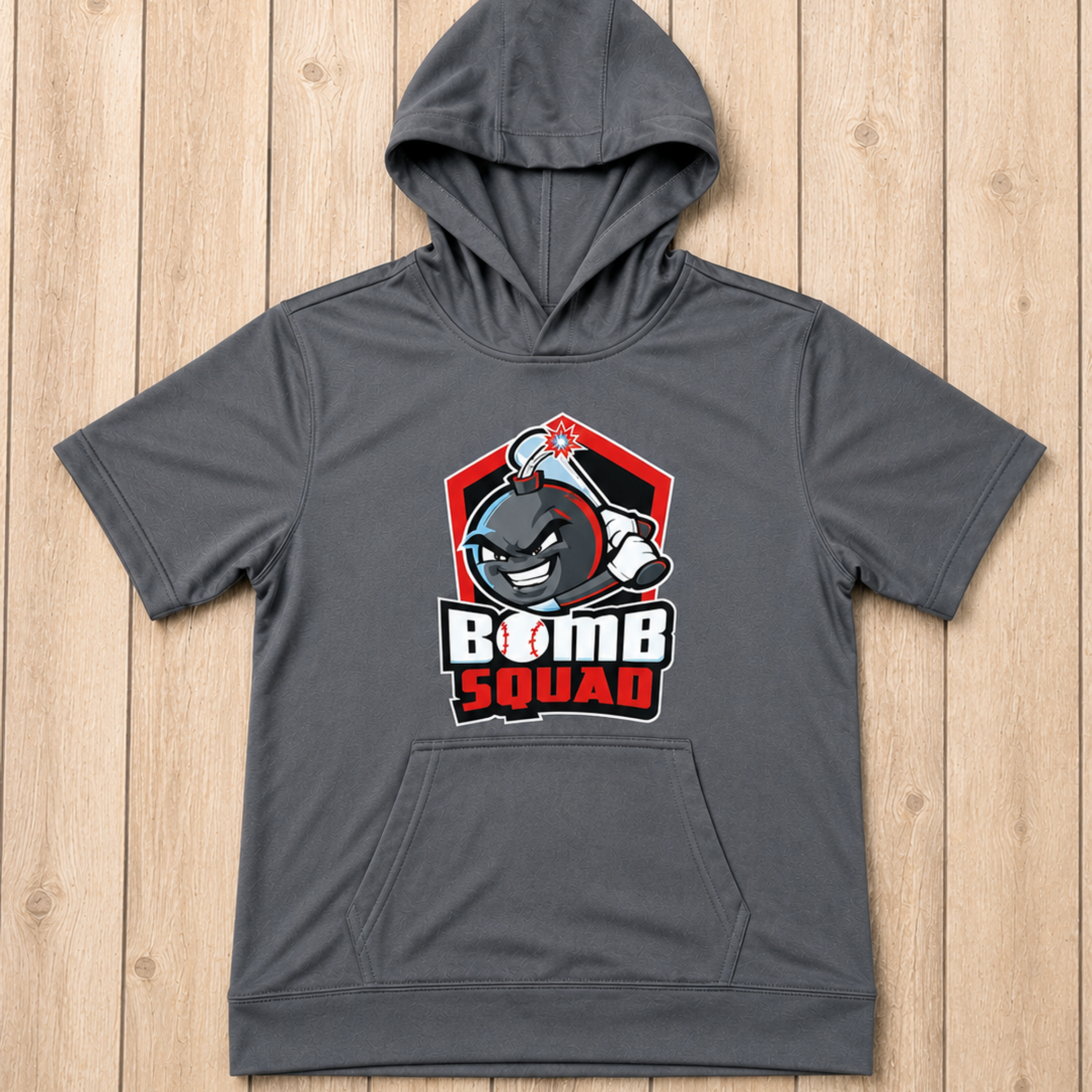 A dark gray short-sleeve hoodie with a front kangaroo pocket and a 'Bomb Squad' graphic on the chest, laid flat on a light wood plank background.