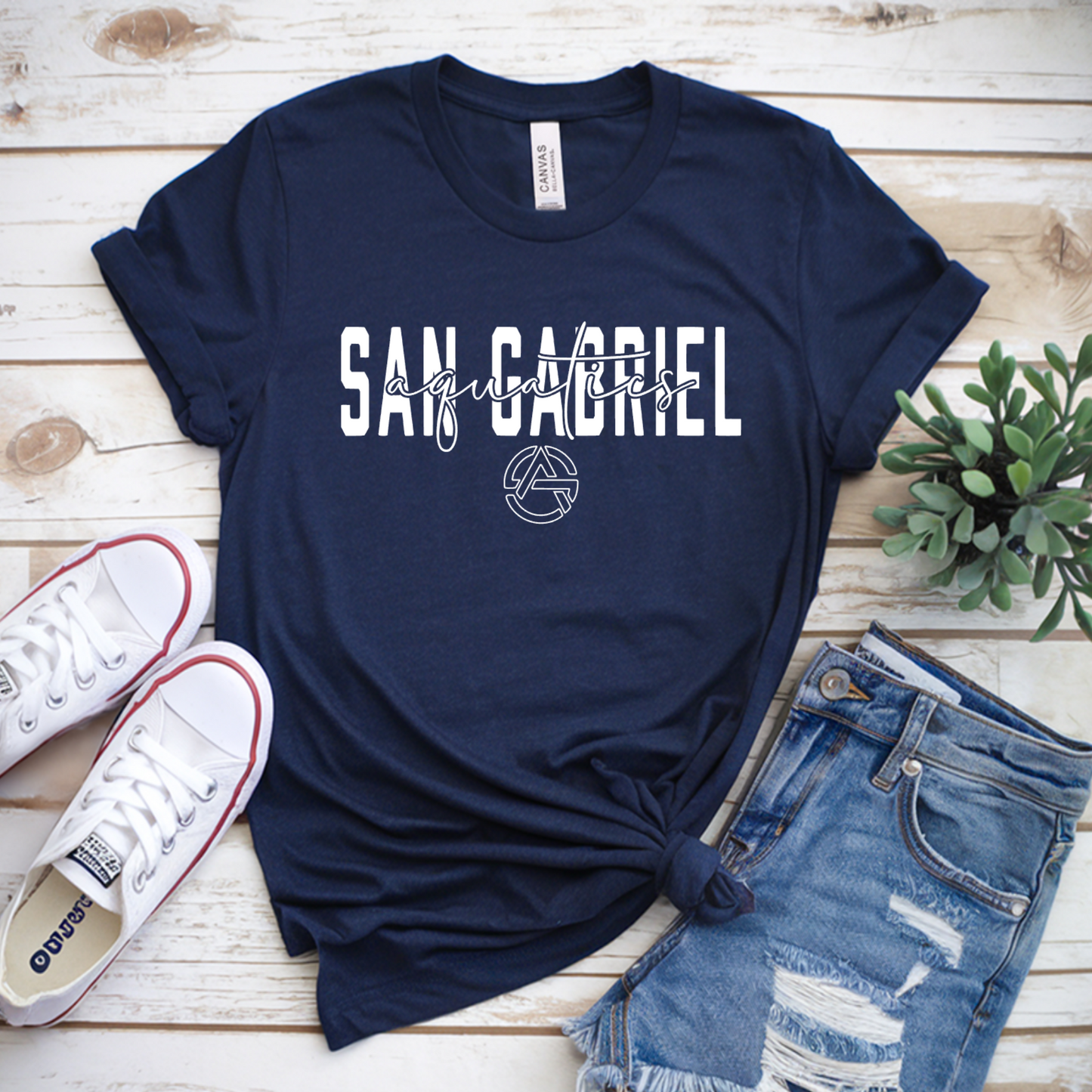 Navy blue t-shirt with 'San Gabriel' print on a wooden surface with sneakers and shorts.