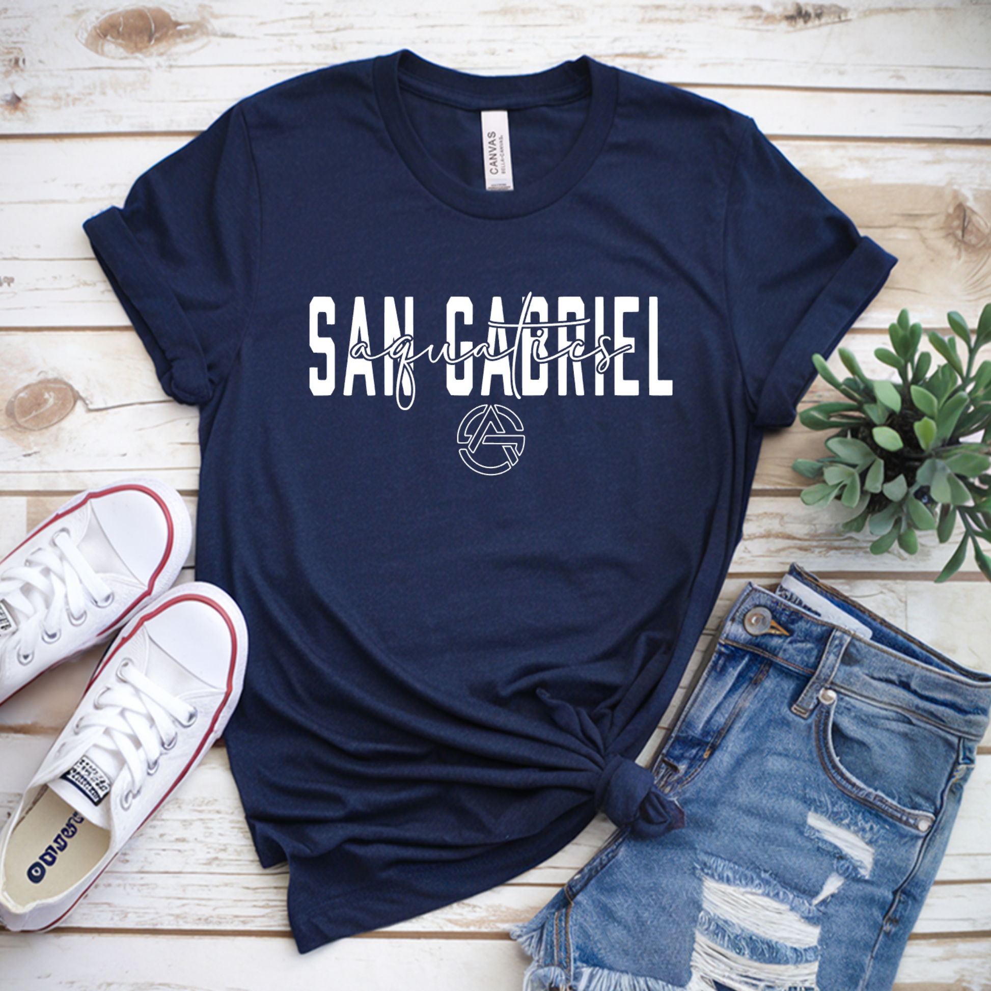 Navy blue t-shirt with 'San Gabriel' print on a wooden surface with sneakers and shorts.