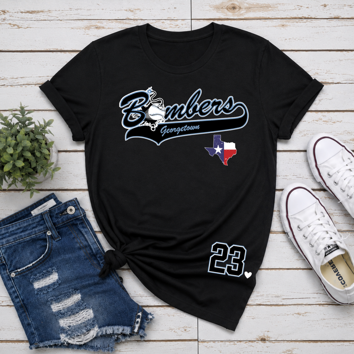 Black t-shirt with 'Bombers Georgetown' design, denim shorts, and white sneakers on a wooden surface.