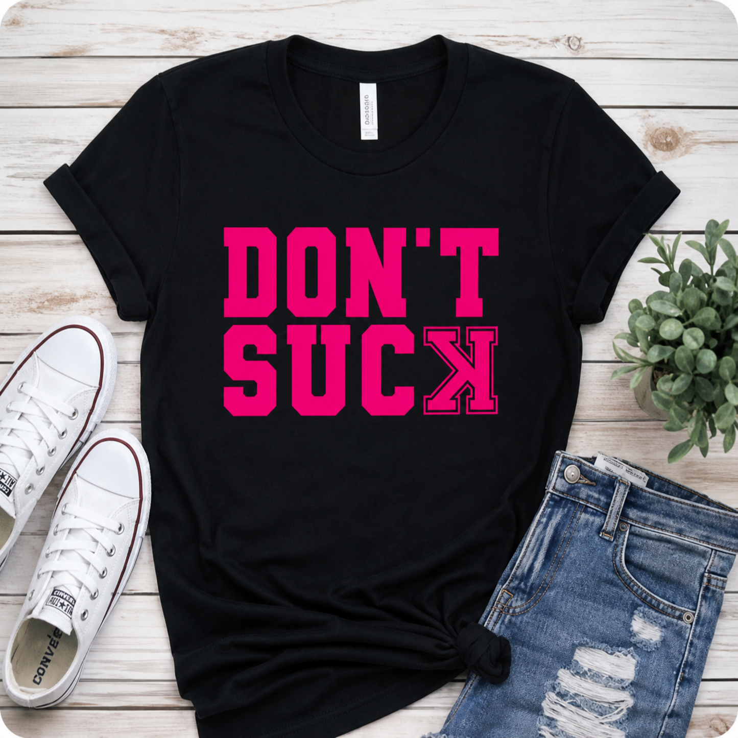 Black t-shirt with pink text 'DON'T SUCK', white sneakers, and blue jeans on a wooden surface.