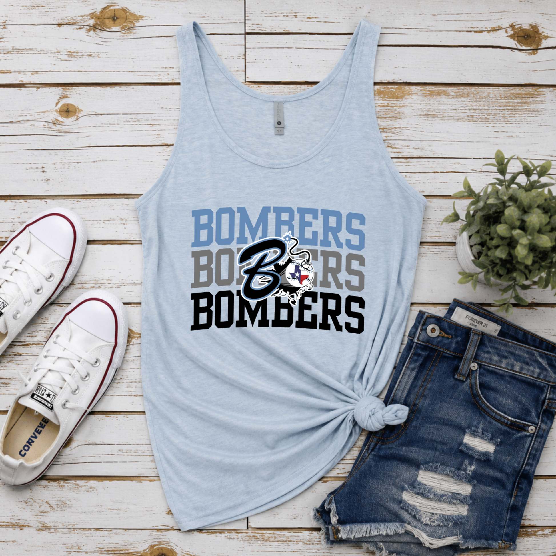 Light blue tank top with 'Bombers' text, denim shorts, white sneakers, and a plant on a wooden surface.