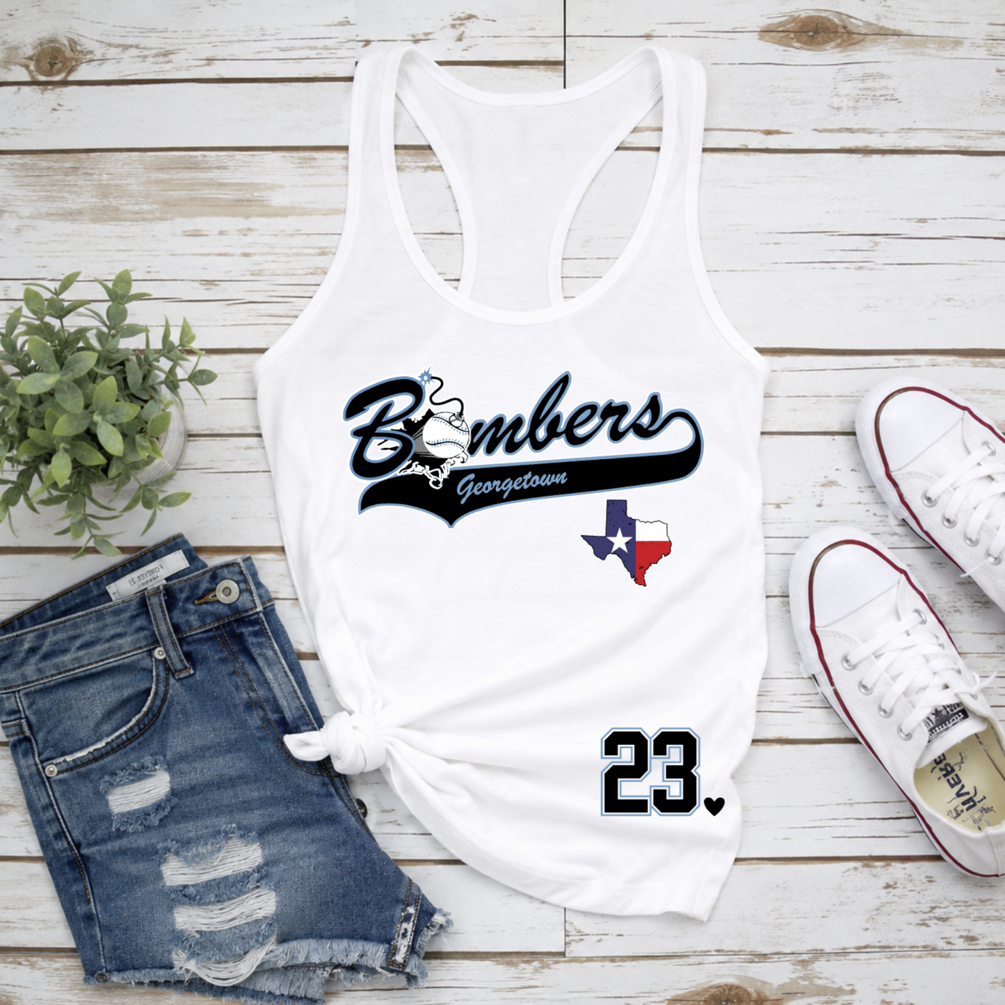 White tank top with 'Bombers Georgetown' text, denim shorts, and white sneakers on a wooden surface.