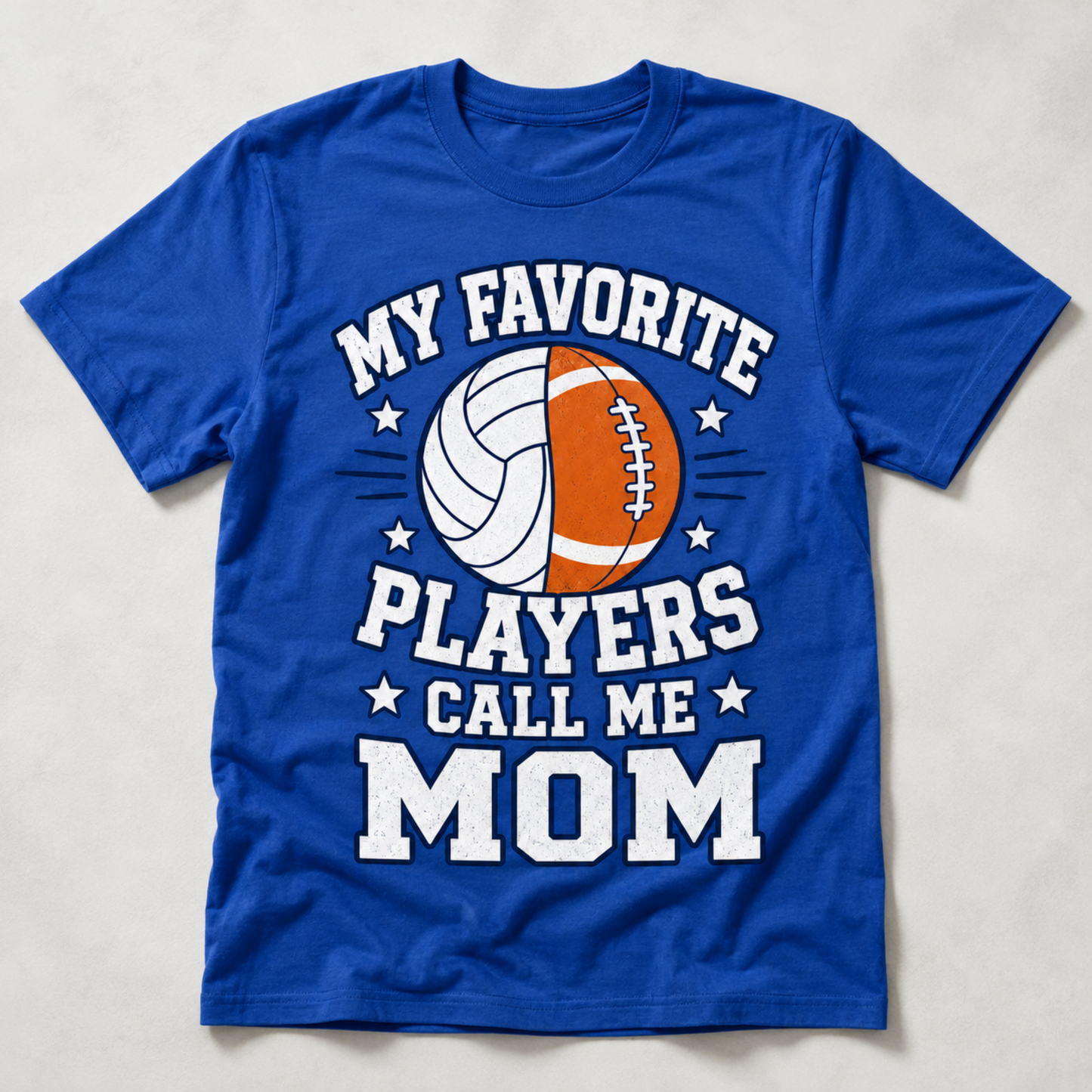 A royal blue short-sleeve t-shirt with a graphic print on the front that reads 'MY FAVORITE PLAYERS CALL ME MOM' in white block letters, surrounding a split sports ball design in white and orange. The t-shirt is laid flat on a light gray textured background.