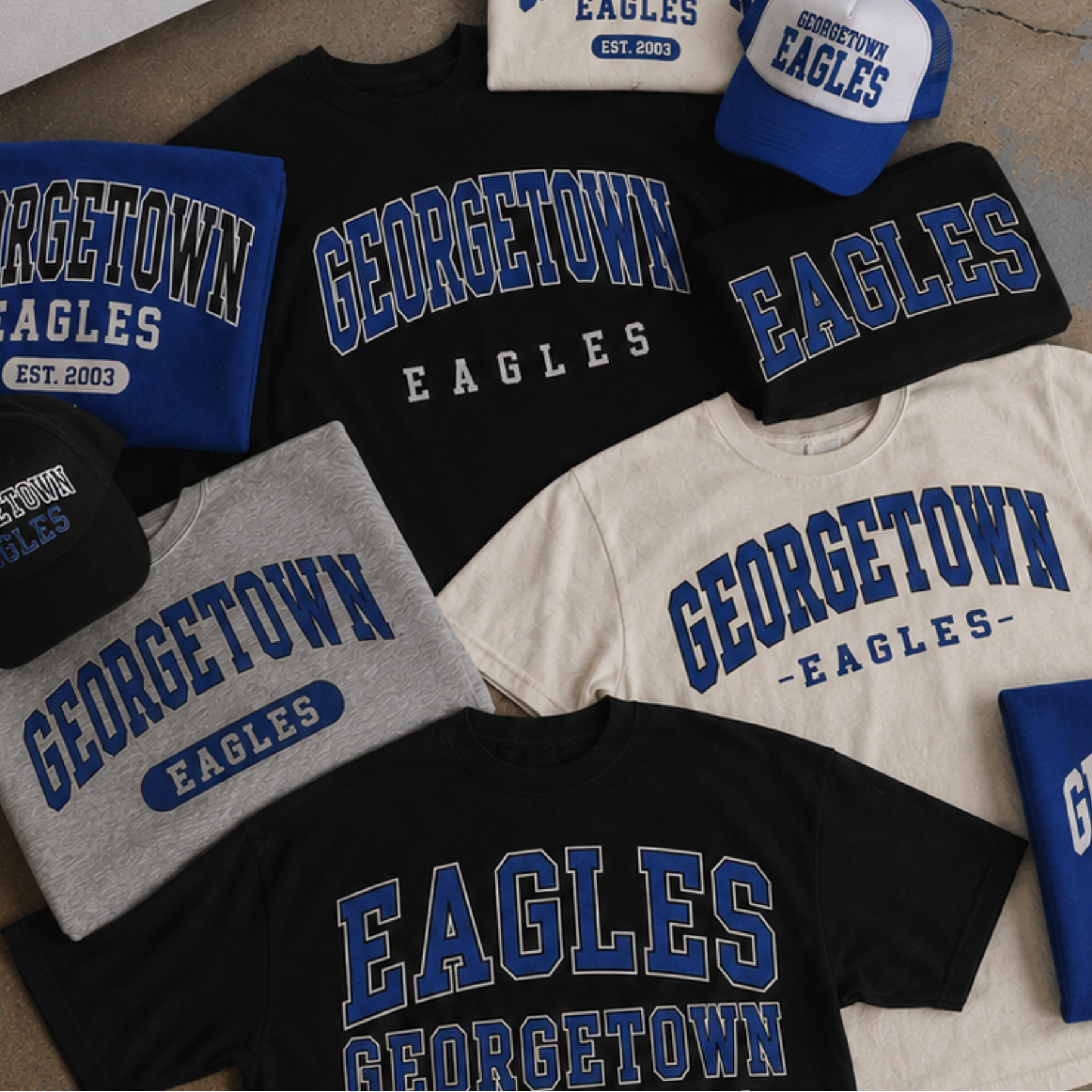 Collection of Georgetown Eagles merchandise including t-shirts, hats, and a bag on a concrete floor.