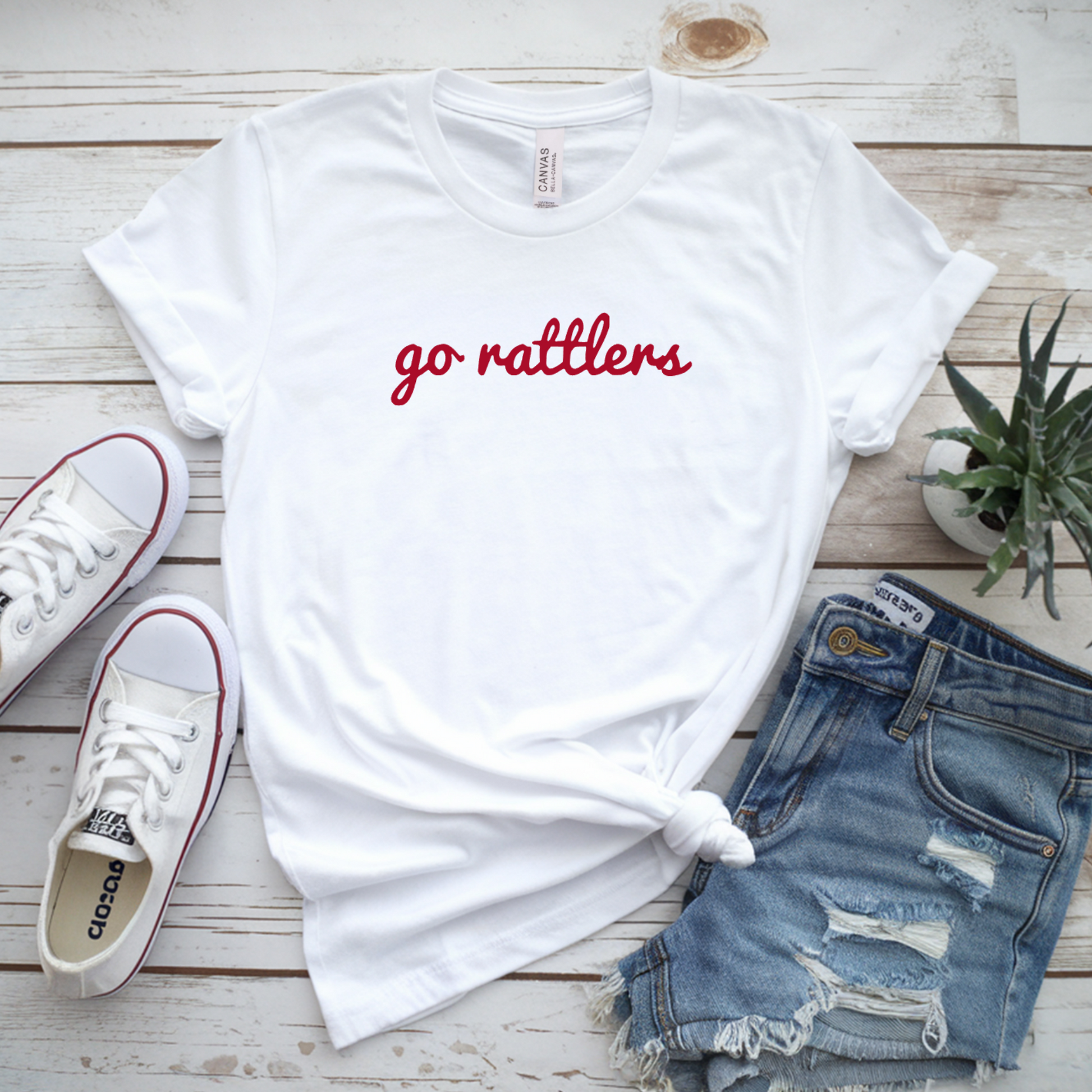 White t-shirt with 'go rattlers' text, Converse shoes, denim shorts on a wooden surface.