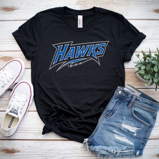 A black graphic t-shirt with 'HAWKS' in blue and white lettering, styled in a flat lay with distressed denim shorts, white canvas sneakers, and a small potted succulent on a white wood plank background.