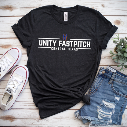 Black t-shirt with 'Unity Fastpitch Central Texas' text, white sneakers, and denim shorts on a wooden surface.