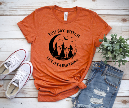 Orange t-shirt with Halloween graphic and text, paired with white sneakers and ripped jeans on a wooden surface.