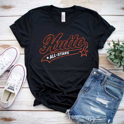 Black t-shirt with 'Hutto All-Stars' design, white sneakers, denim shorts, and a plant on a wooden surface.
