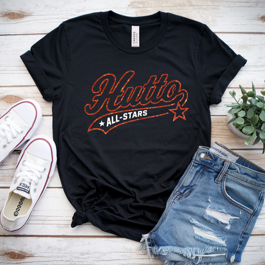 Black t-shirt with 'Hutto All-Stars' design, white sneakers, denim shorts, and a plant on a wooden surface.