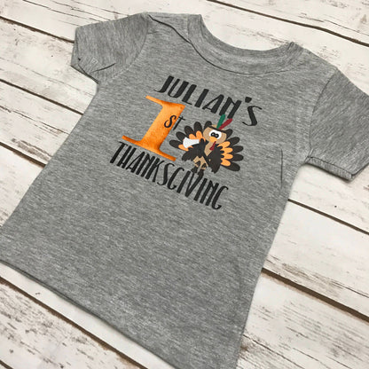 Gray t-shirt with 'Julian's 1st Thanksgiving' design on a wooden surface