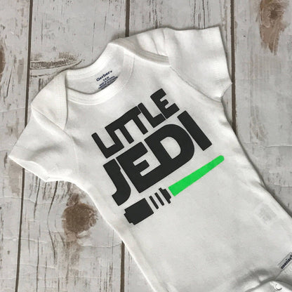 White baby onesie with 'Little Jedi' print on a wooden surface