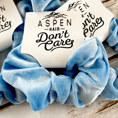 Blue scrunchie with 'Aspen Hair Don't Care' text on a wooden surface