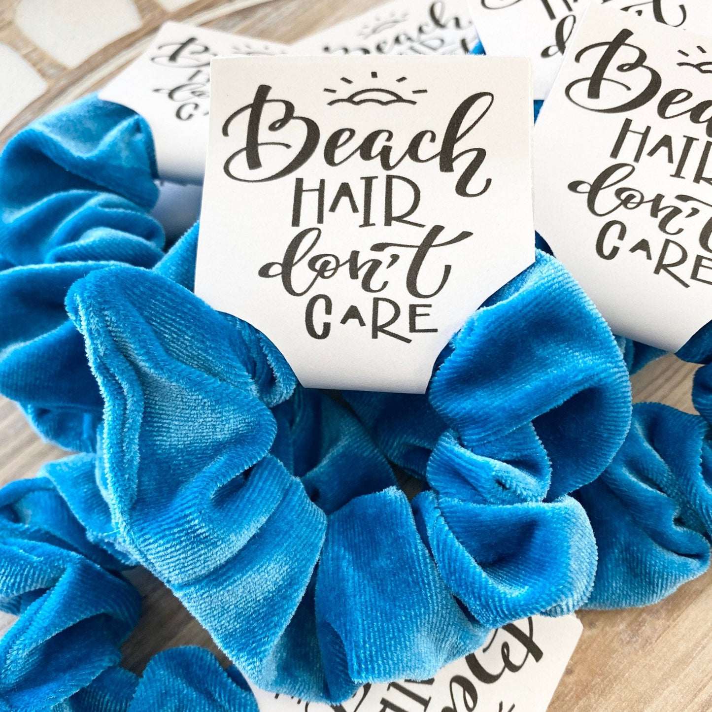 Blue scrunchies with 'Beach Hair Don't Care' cards on a wooden surface