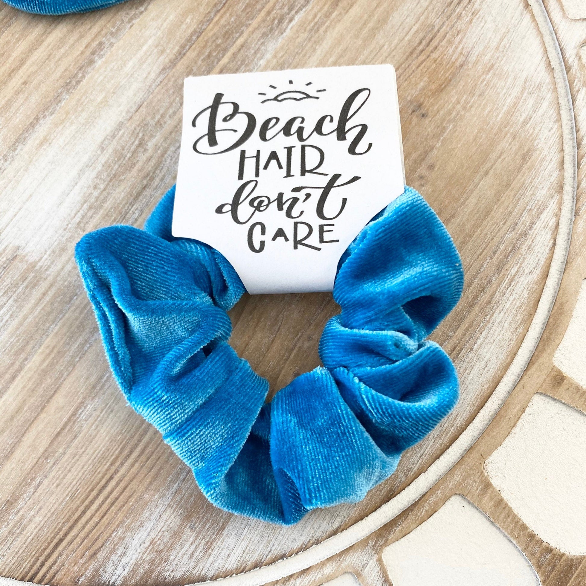 Blue scrunchies with a 'Beach Hair Don't Care' sign on a wooden surface