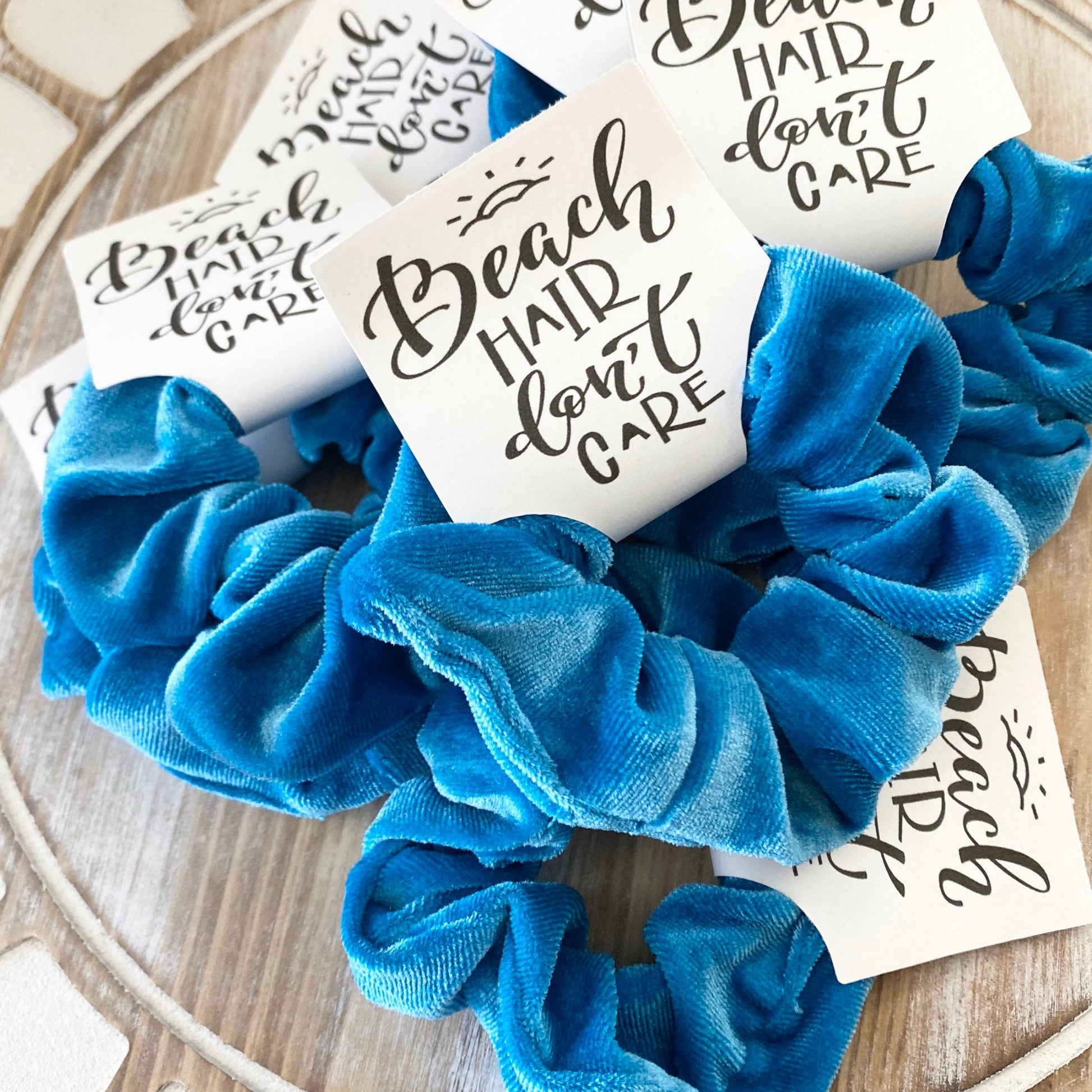 Blue scrunchie with 'Beach Hair Don't Care' cards on a wooden surface