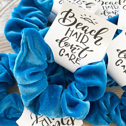 Blue scrunchies with 'Beach Hair Don't Care' cards on a wooden surface