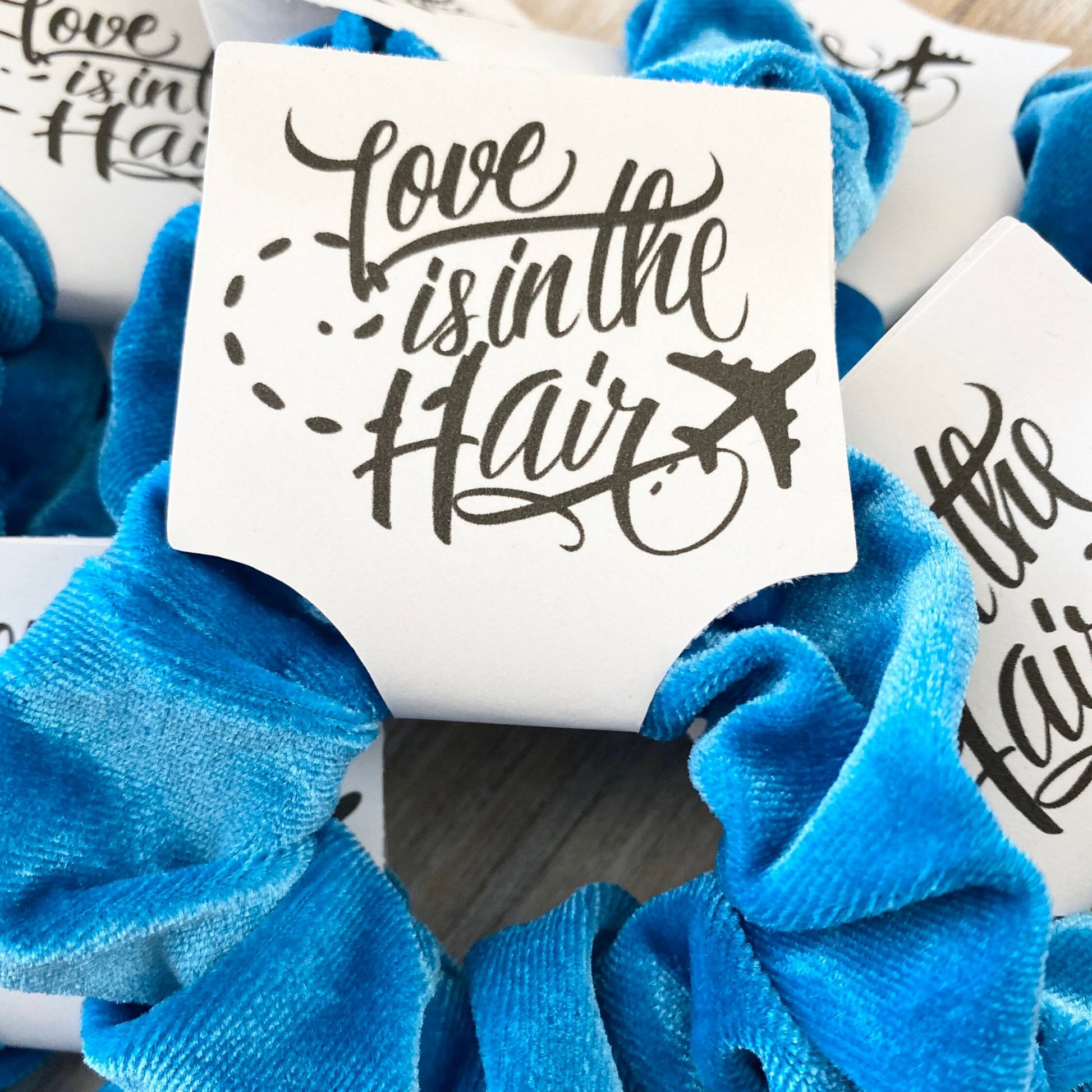 Blue scrunchies with 'Love is in the Hair' text on white cards.