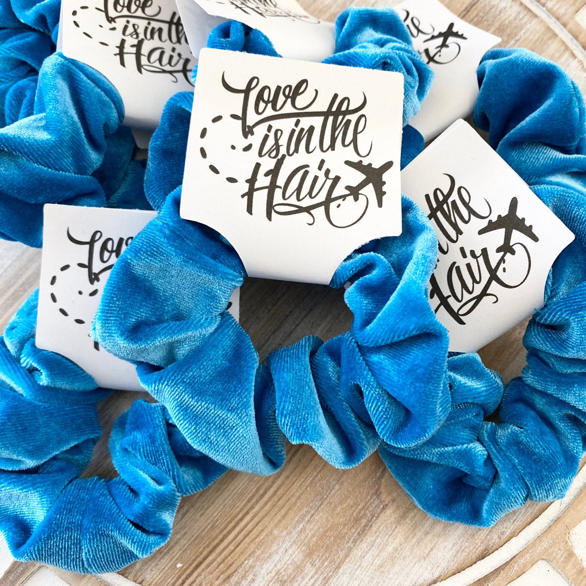 Blue scrunchies with 'Love is in the Hair' cards on a wooden surface