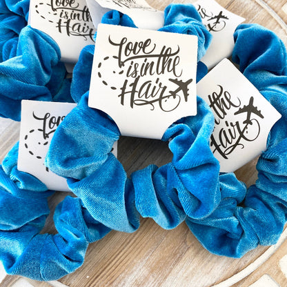 Blue scrunchies with 'Love is in the Hair' cards on a wooden surface